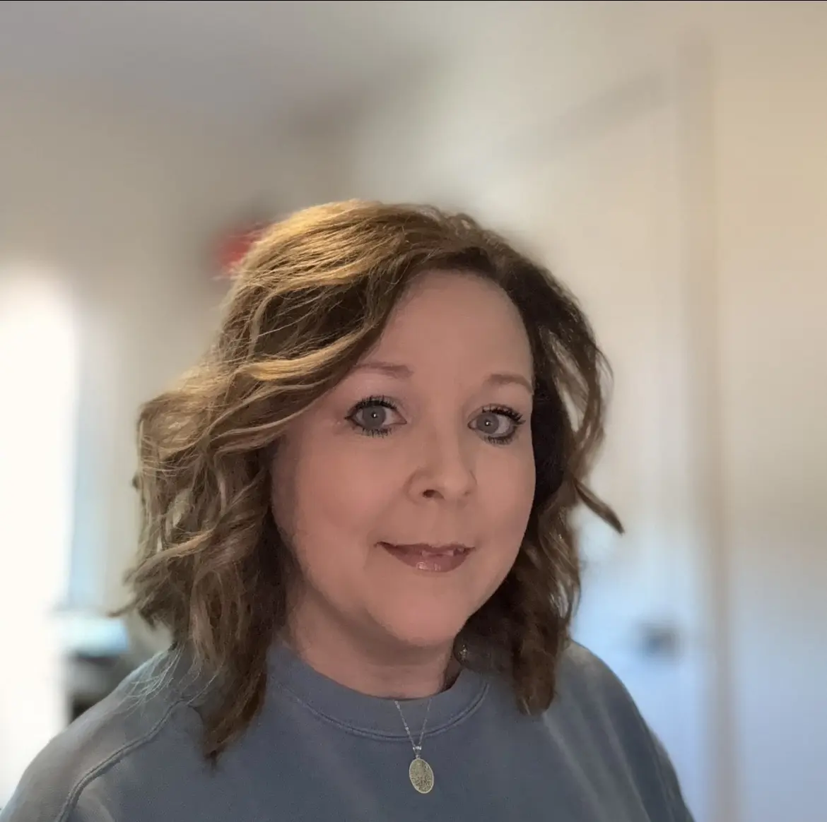 Smiling woman with wavy hair in a softly lit room.