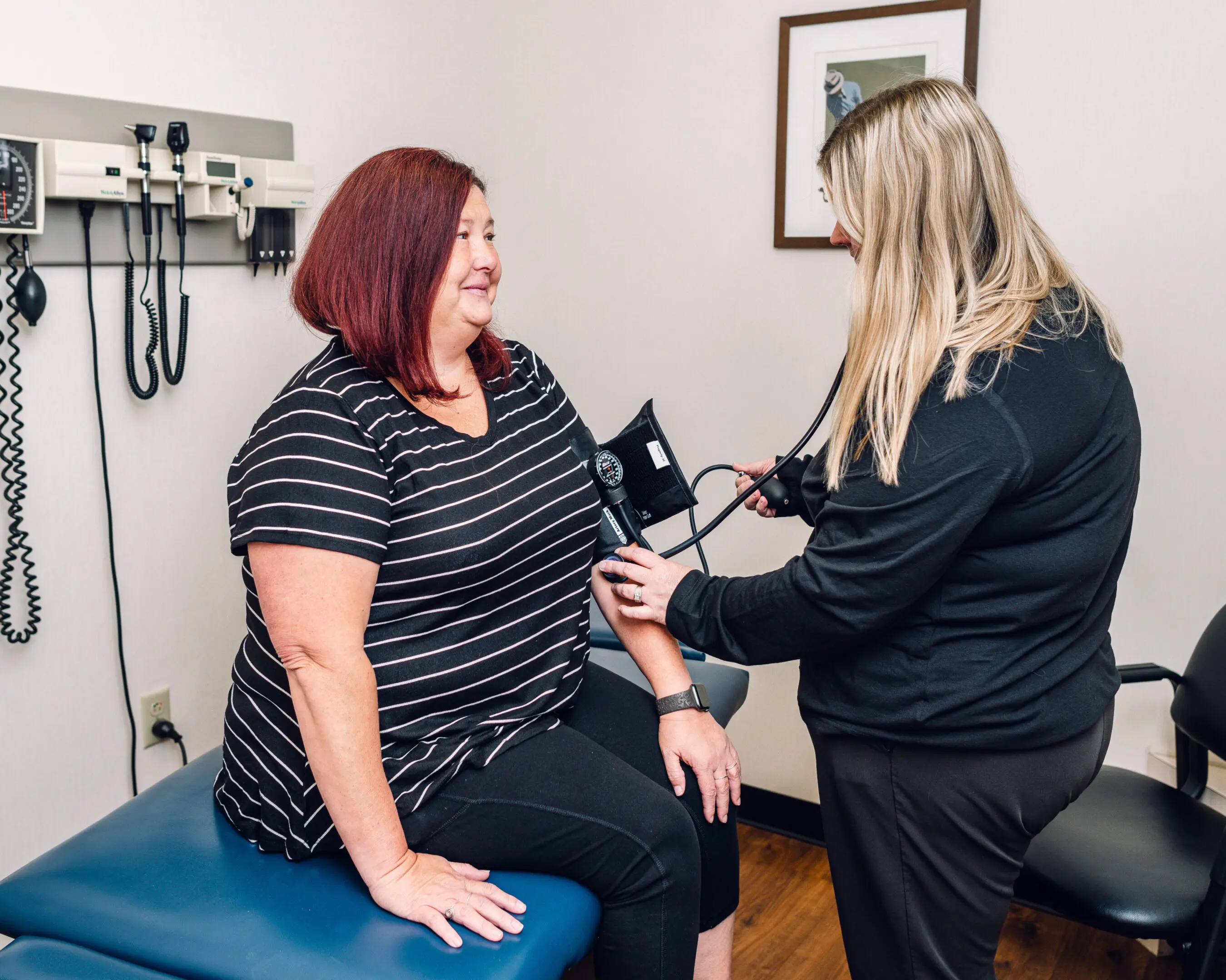 Nurse measuring blood pressure of a seated woman in a clinic.