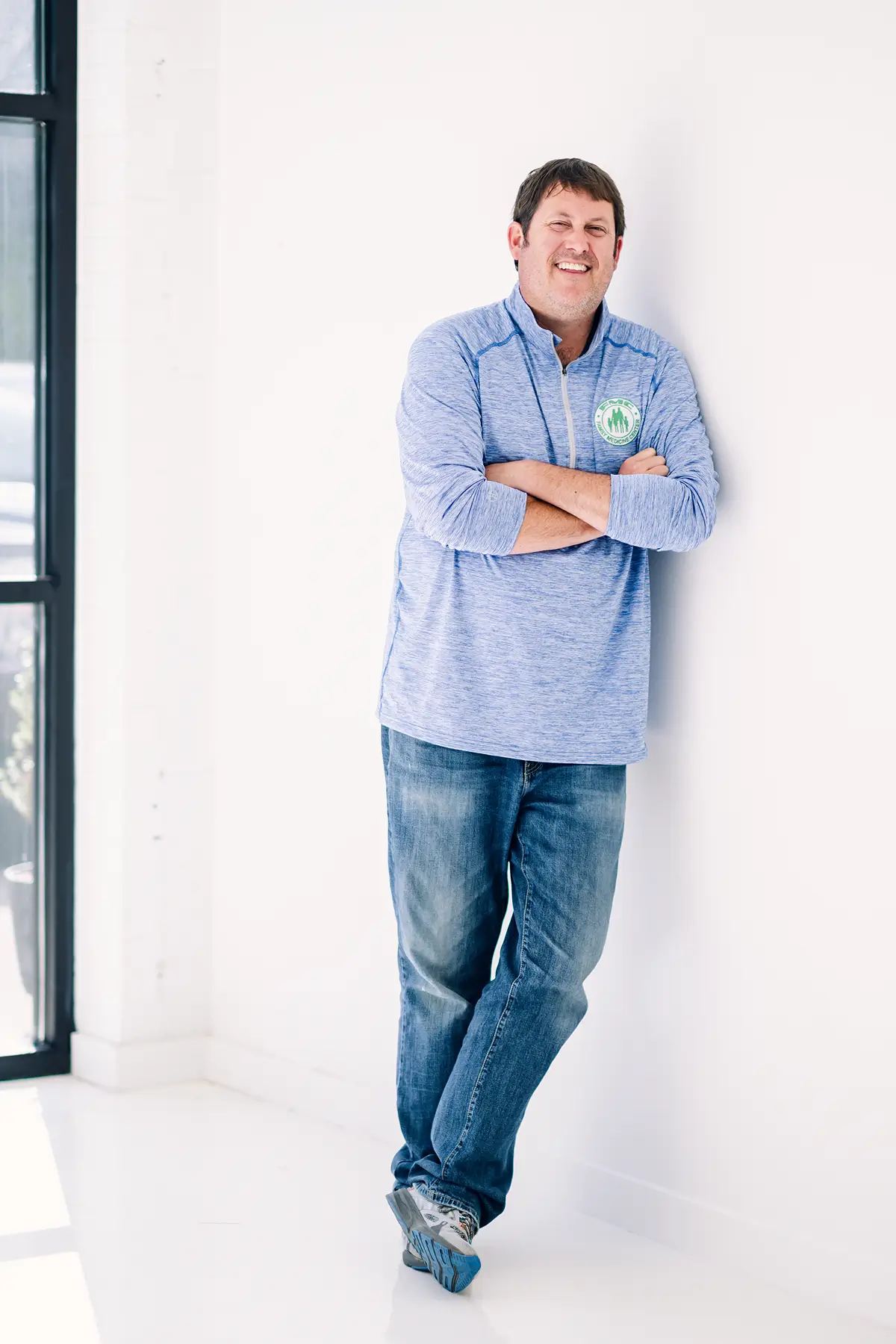 Man leaning against white wall, smiling.