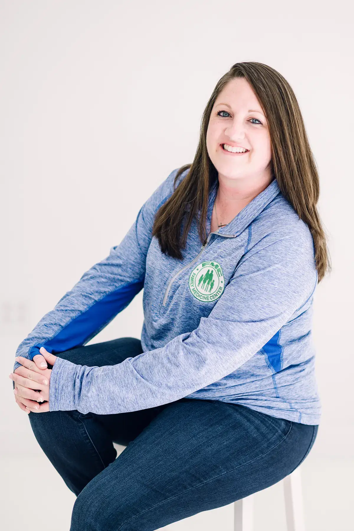 Smiling woman in blue sitting on stool.